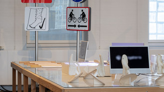 Exhibition with traffic signs, models, and a screen on a large wooden table.