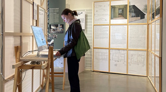 Kvinde ser på computerskærm på en baggrund af udstillede plancher