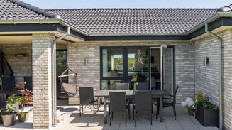 Moderne murstenshus med overdækket terrasse og havemøbler.
