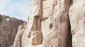 Monumentalt klippehugget relief i en sandstensklippe med få besøgende ved foden.