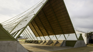 Åben pavillon med højt skråt tag over en udendørs bane.