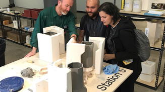 Three people examine ceramic forms together in a workshop.