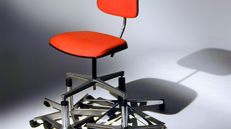 Red office chair stands atop a pile of wheeled chair bases.
