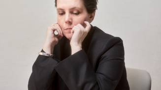 Woman in black sits at a table with her chin resting in her hands.
