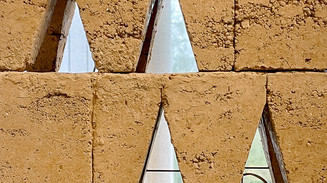 Sandfarvet facade med geometriske, trekantede åbninger.