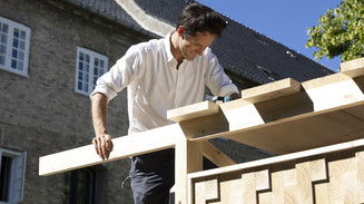 Man on a ladder works on the roof of a wooden structure.