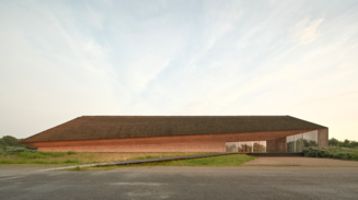 ong, low building with a thatched roof, red earthen walls, and a glass façade in an open landscape.