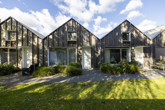  Små træbeklædte huse med private indgange og grønne arealer foran.