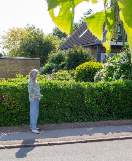 Woman researcher standing in front of a green hedge and a yellow brick house