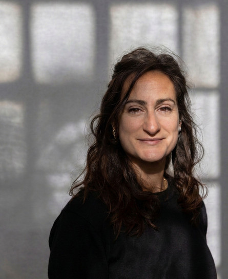 Picture of Roberta with shoulder-length brown hair and fair skin, wearing a light-colored t-shirt, looking directly at the camera with a neutral expression against a soft, light background.