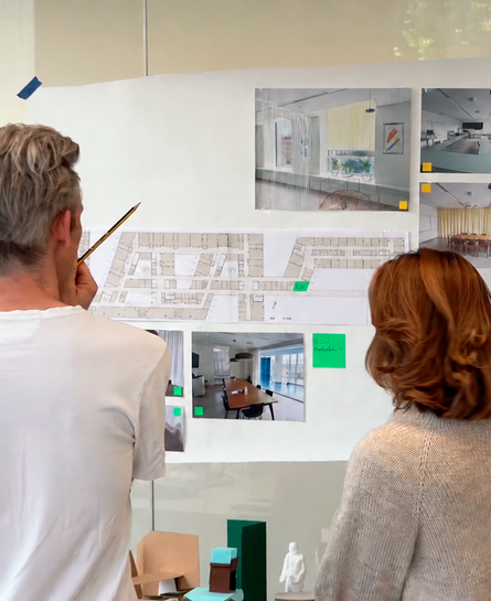 Fire personer studerer plantegninger og visualiseringer af indretning på en væg.