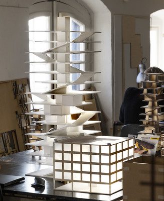 Arkitekturmodeller står på arbejdsborde i et lyst modelværksted.