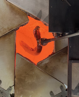 Glødende glas formes på en pibe foran en åben glasovn.