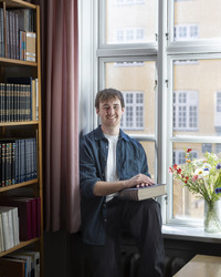 James sitting by the window in a library, with a book in his hands.