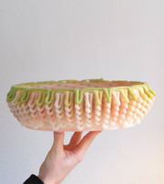 Hand holding a bowl-shaped object layered with glossy loops in pastel colors.