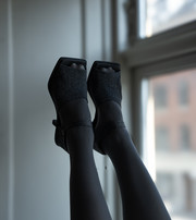Feet in black open-toe high-heeled dance shoes raised in front of a window.
