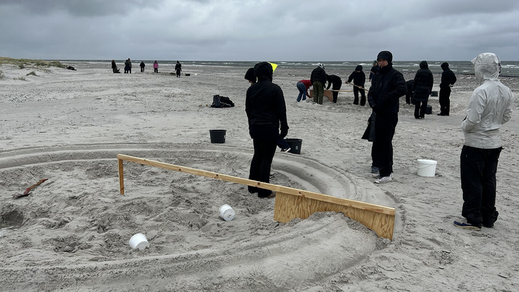 Studerende på strand, sandcirkel i forgrunden
