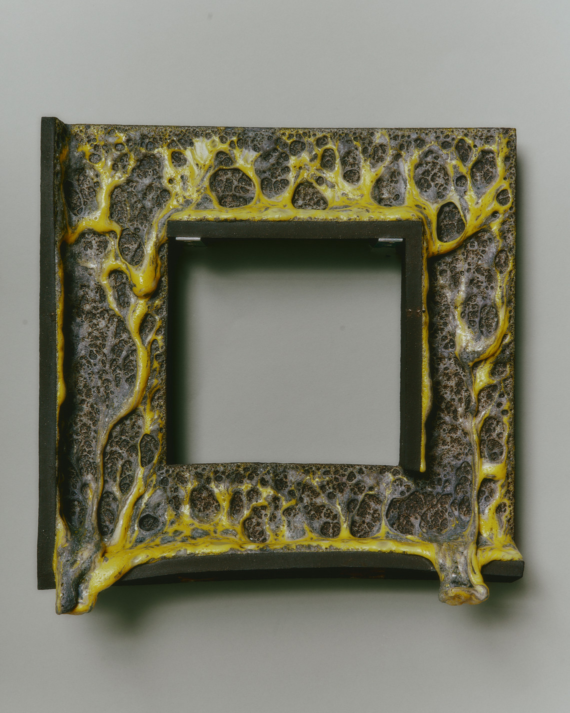 square ceramic object, yellow and grey volcanic glaze spilling over the bottom edge