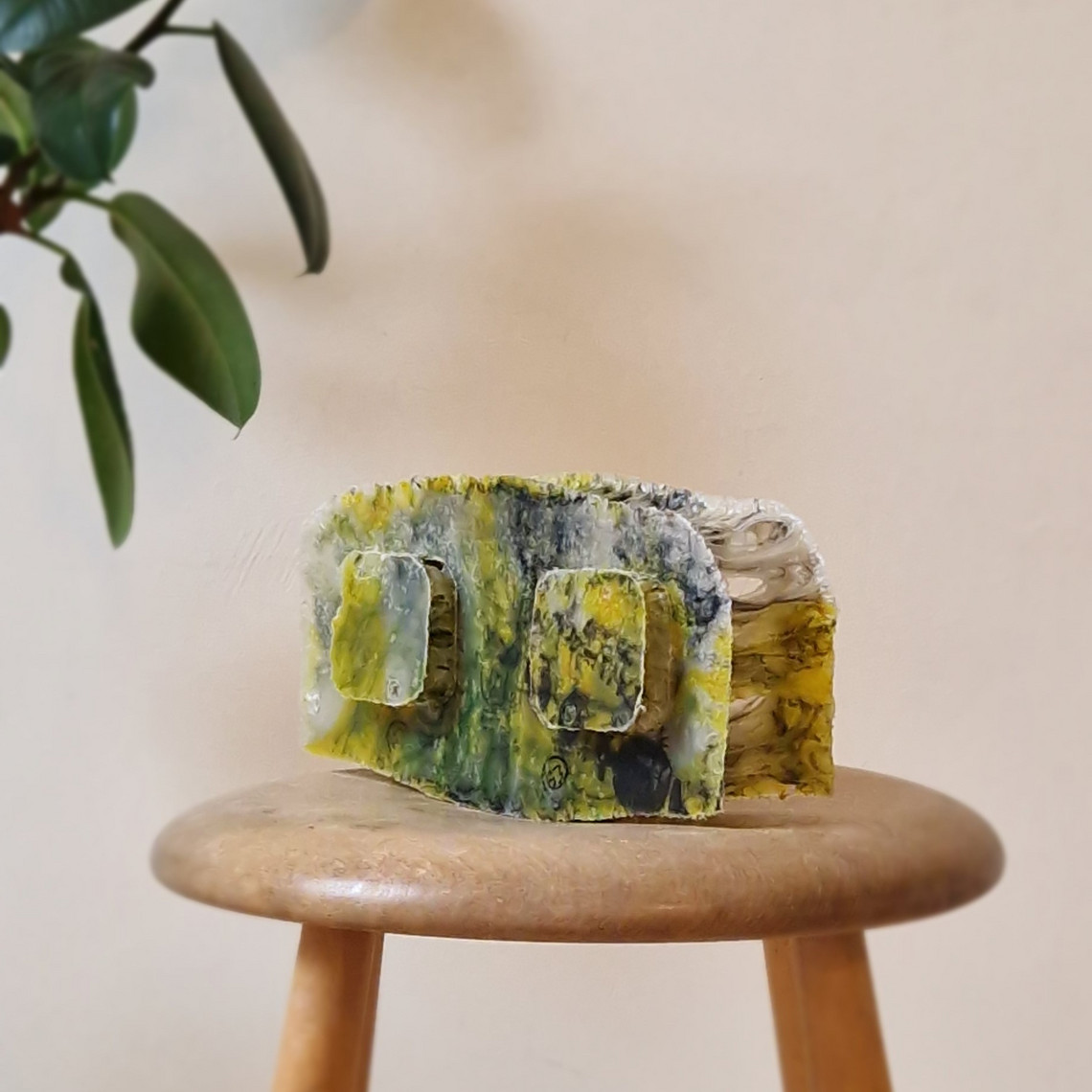 Small textured lump in yellow and green on a wooden stool.