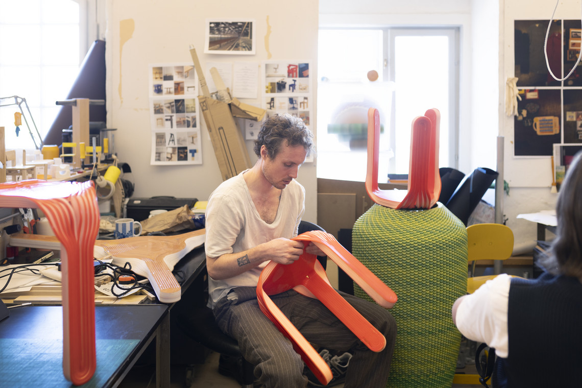 Person shaping bright red chair parts in a workshop.
