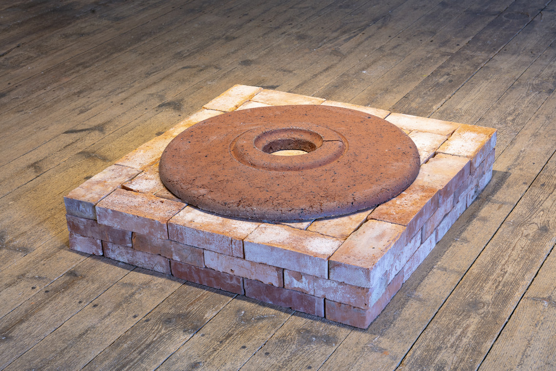 Square brick structure with circular rusted disk on top.