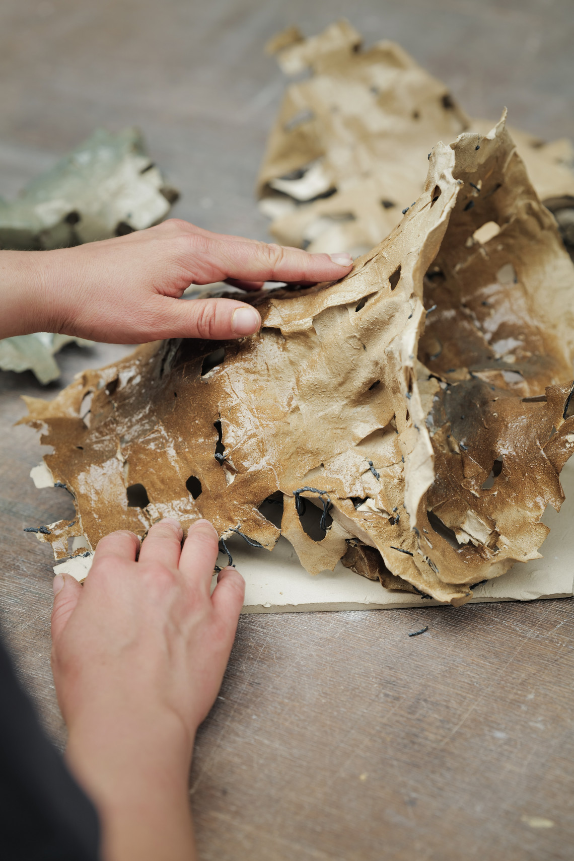 Hands shaping a perforated clay piece on a worktable.