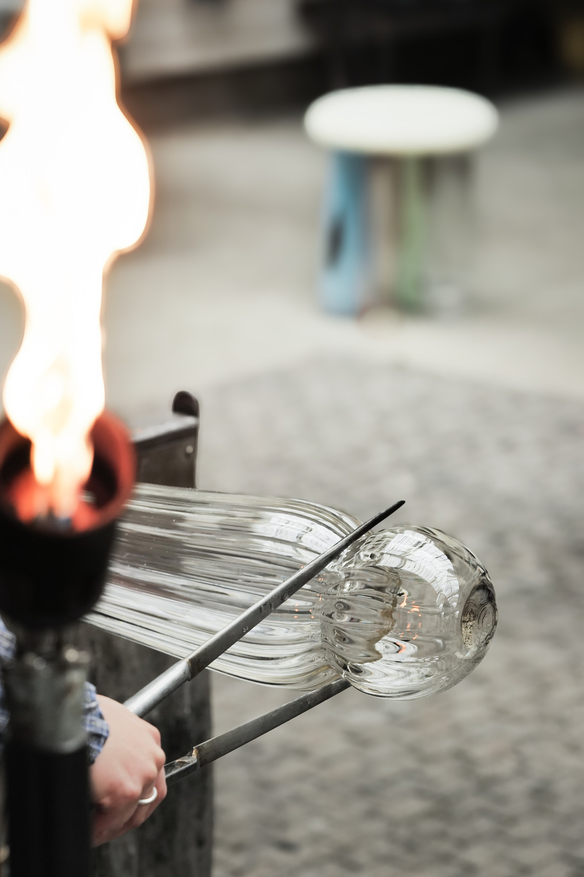 Glassblower heating and shaping molten glass with a flame.