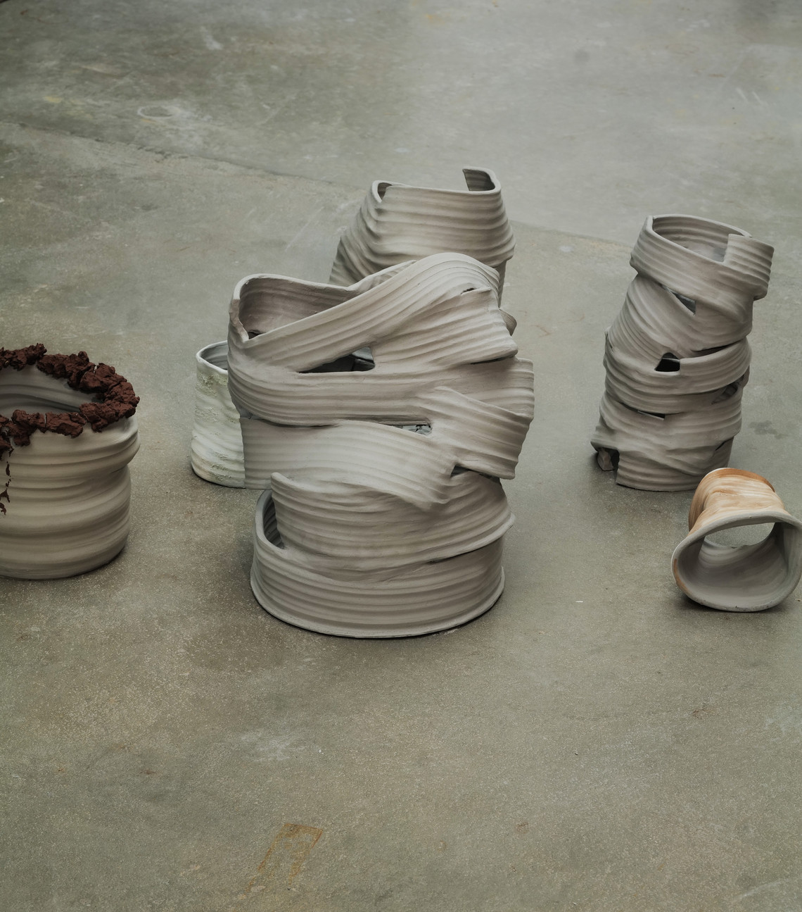 Abstract clay vessels with layered, sculptural surfaces on a floor.