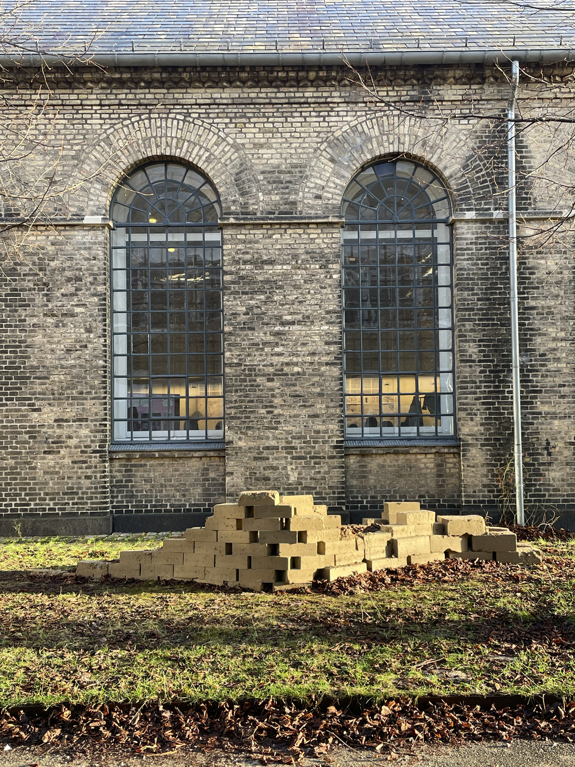 Mud brick structure in front of brick wall with big windows at Holmen Campus