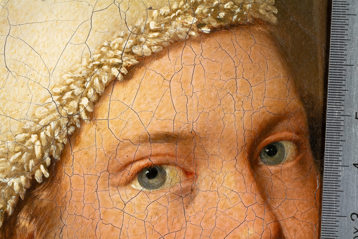 Detail of a cracked painting showing two blue-grey eyes and a ruler along the right edge.
