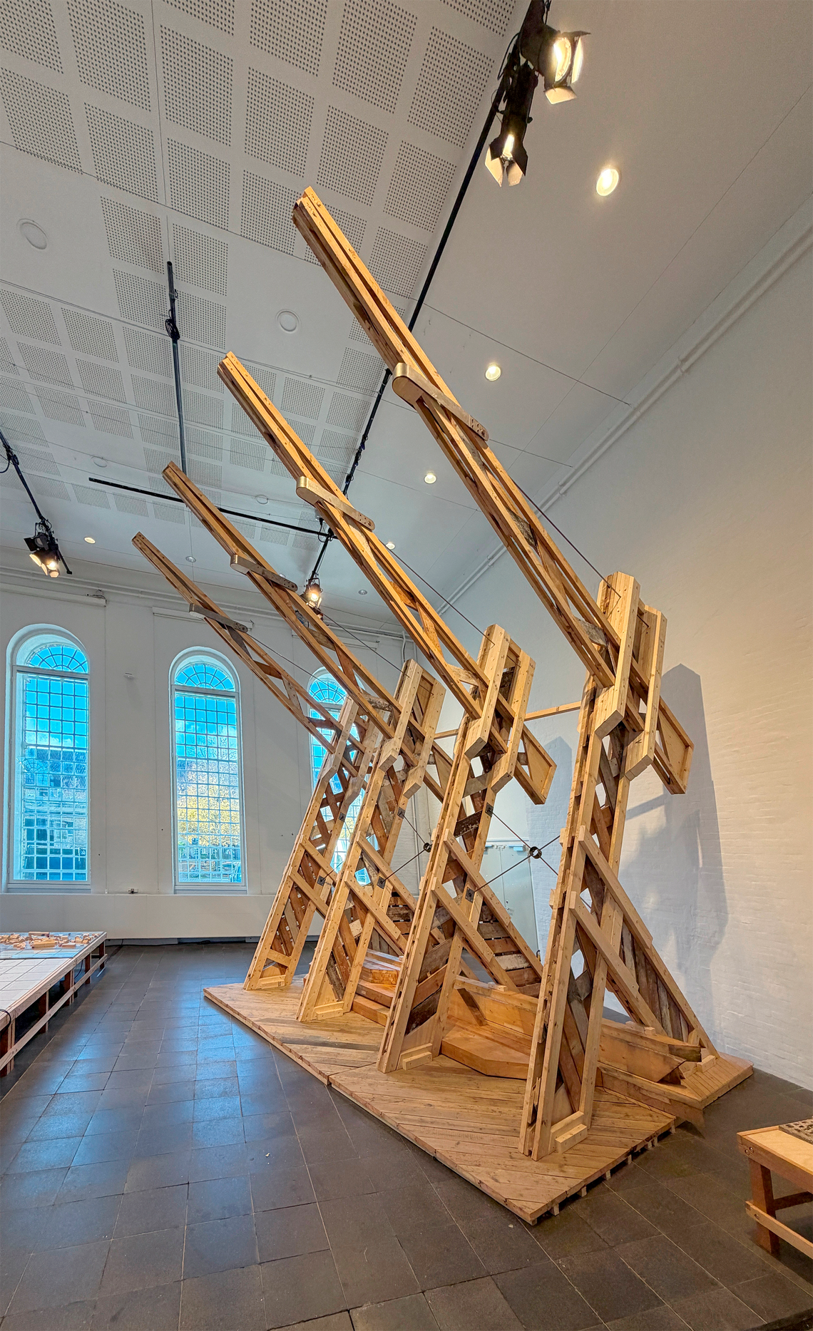 Large installation of angled timber structures with intersecting beams in an exhibition hall.