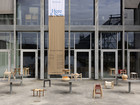 Design exhibition banner on a glass building façade with wooden stools displayed outside.