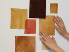 Material samples in warm tones pinned to a wall, with hands touching them.