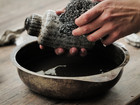 Hands cleaning a ceramic vessel over a bowl of water.