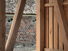 Interior timber structure with diagonal beams overlooking a brick building with a thatched roof.