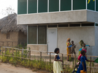Women and children outside a modern two-storey building with green facade panels.