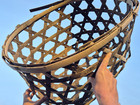 Two hands holding a basket woven from wooden strips against a blue sky.