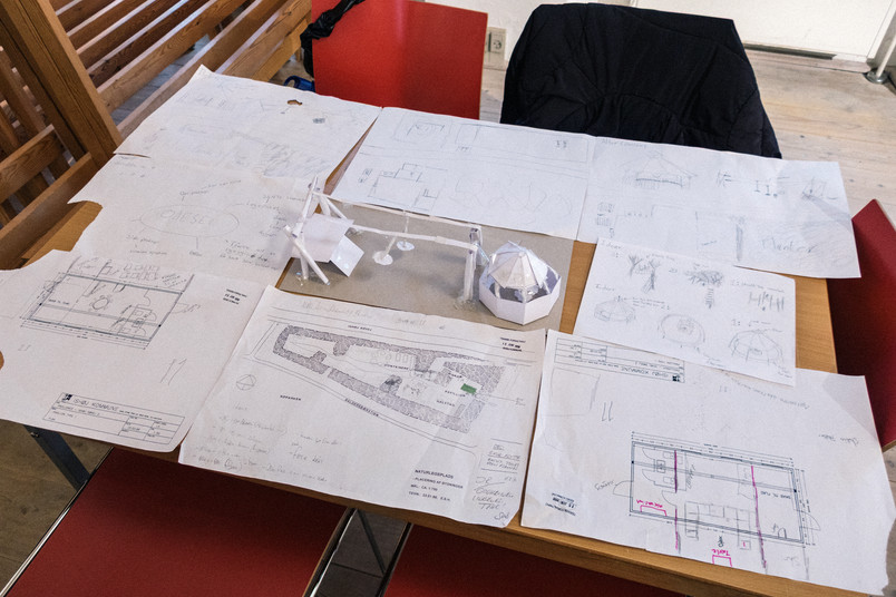 Arkitekturtegninger og lille papirmodel af legeplads på bord