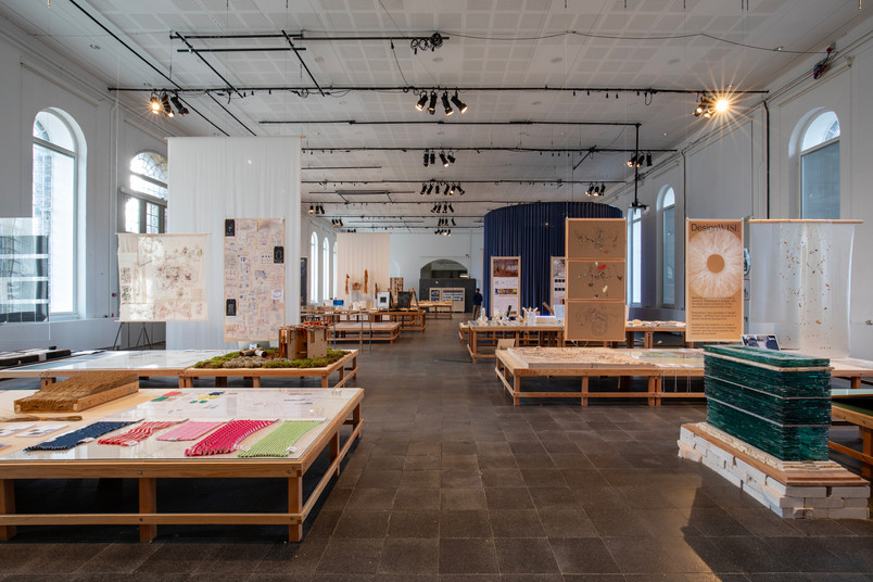 Udstillingsrum med borde fyldt med designprojekter og materialer.