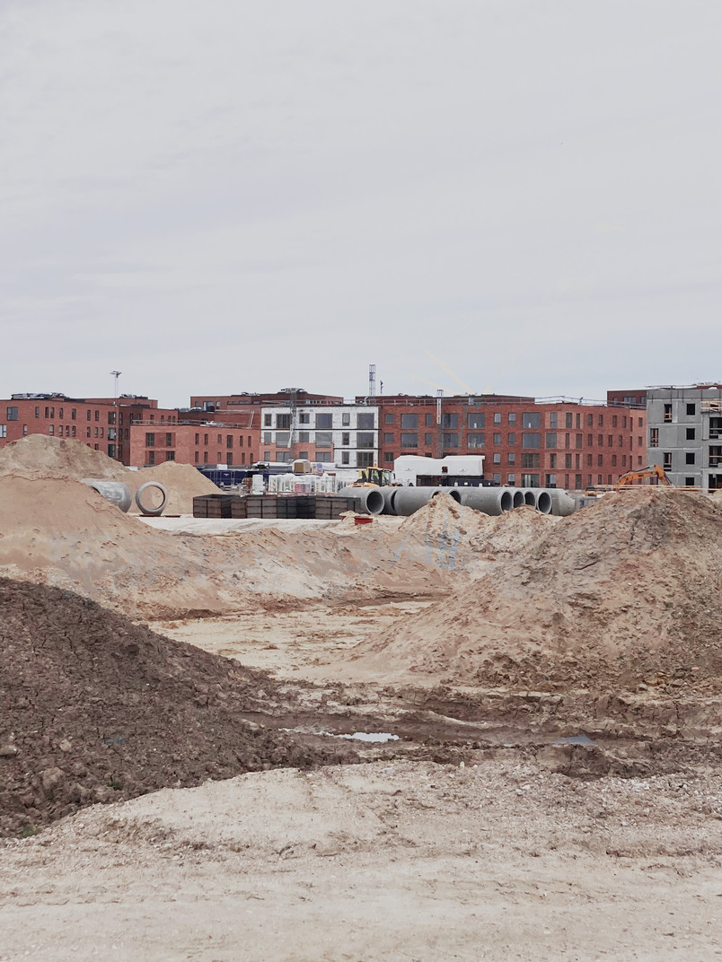 Byggeplads med jordbunker og store betonrør foran nye boligbyggerier.