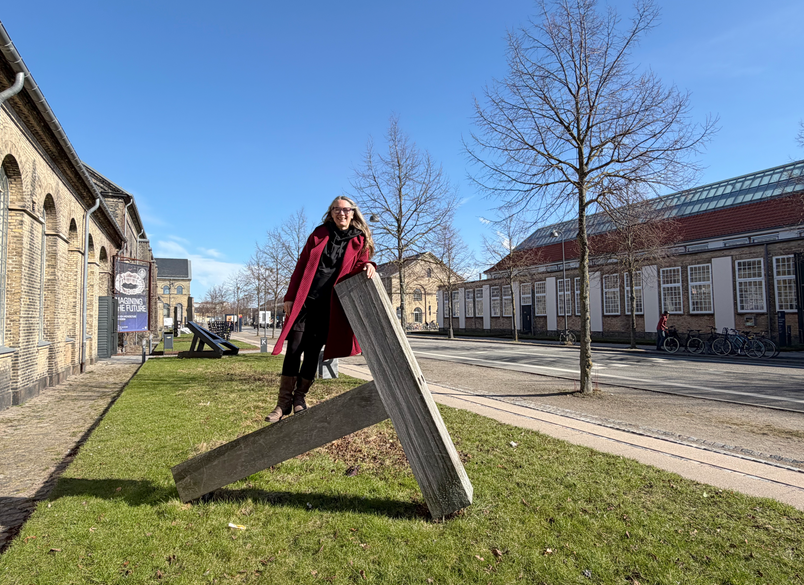 Person står på T-formet skulptur på gade i solskin