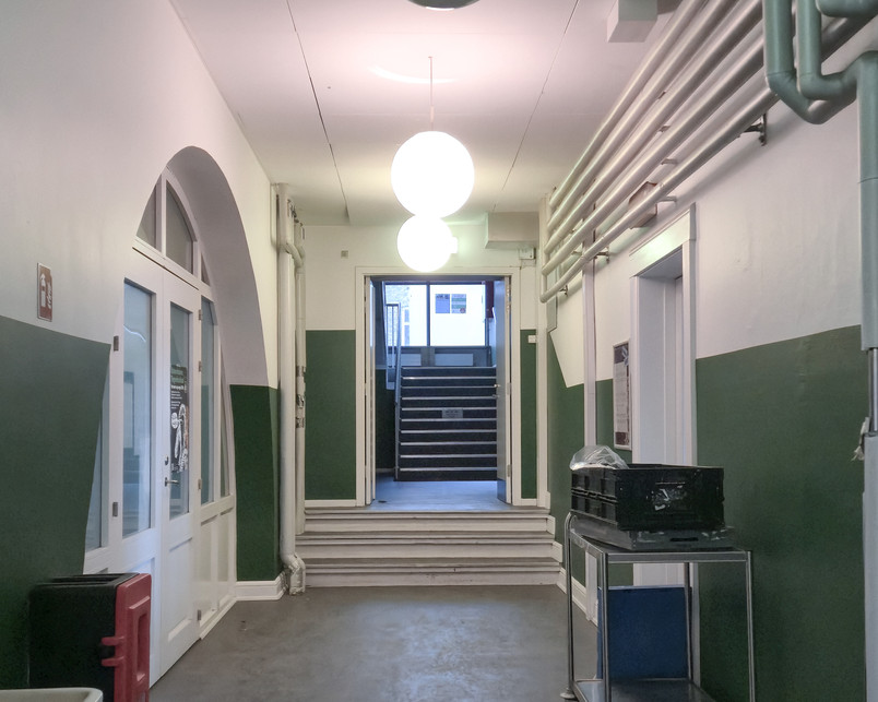 Photo of entrance hallway in the school. As we enter the school, we are faced with tight directionless corridors with painted ­smooth walls and visible piping. In all directions there are steps, which cut the corridors into smaller sections. The halls are quiet at this time and there are no indications of where to go. It feels like we entered a maze.