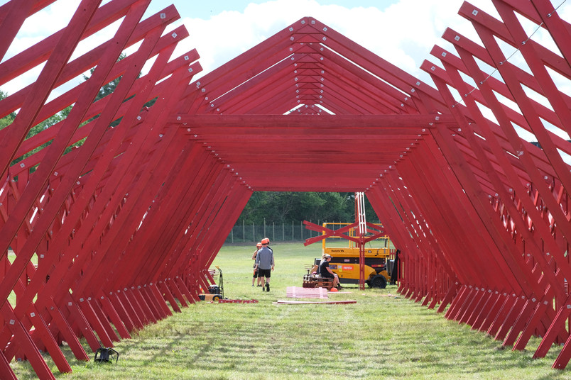 Rød træpavillon under opførelse med arbejdere i baggrunden.