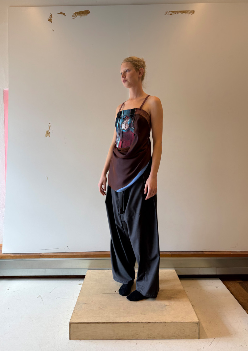 Model wearing a garment inspired by the armour of temple guardian figures, with the image of face-tearing wrathful guardian figure integrated into the surface through a reconstructed armour-like textile technique.