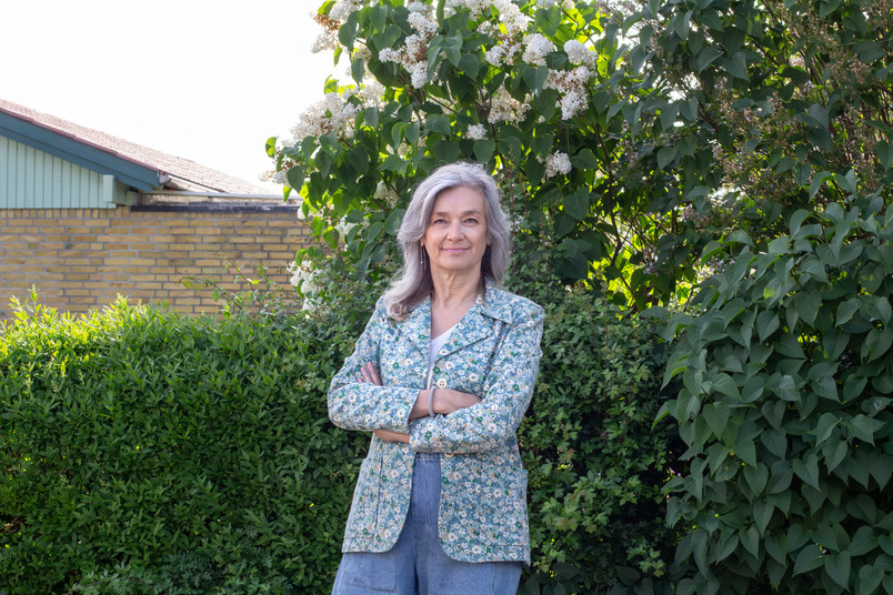 Woman researcher standing in front of a green hedge and a yellow brick house