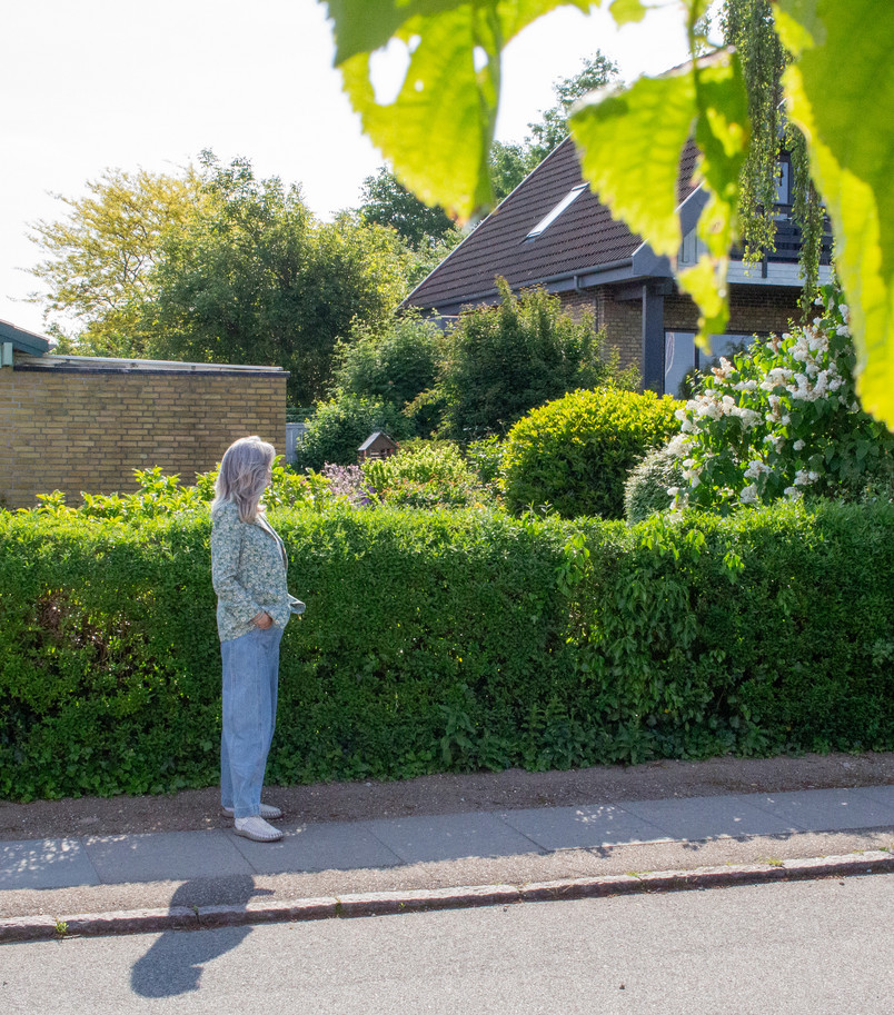 Woman researcher standing in front of a green hedge and a yellow brick house