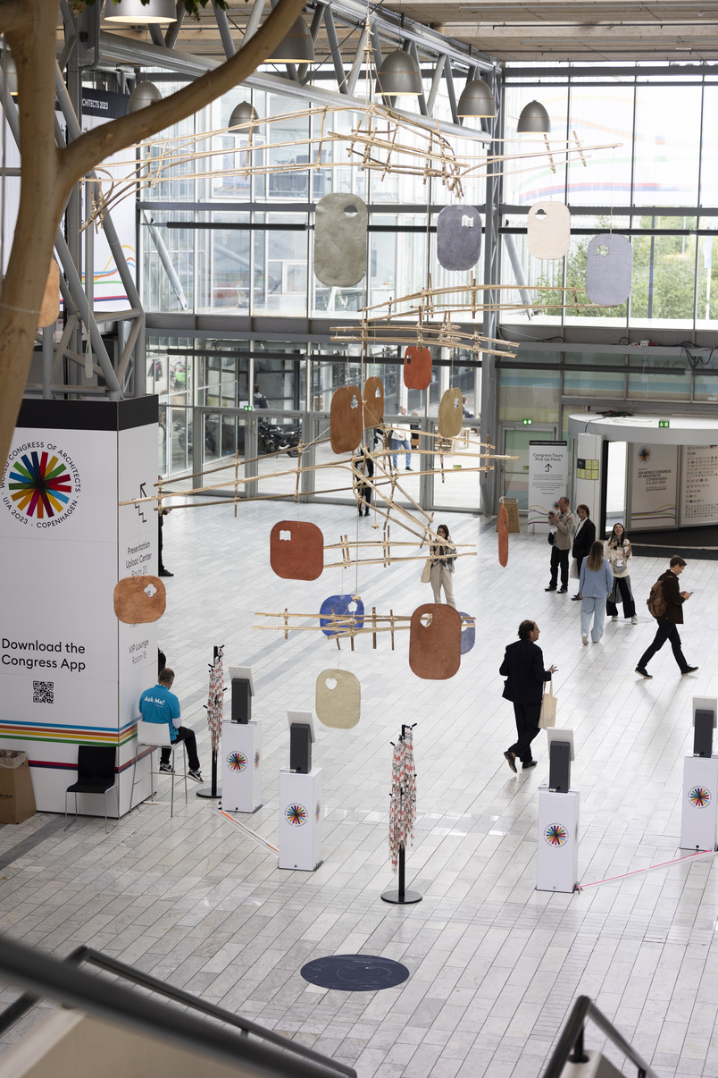 Suspended art installation in a large atrium with visitors walking below.