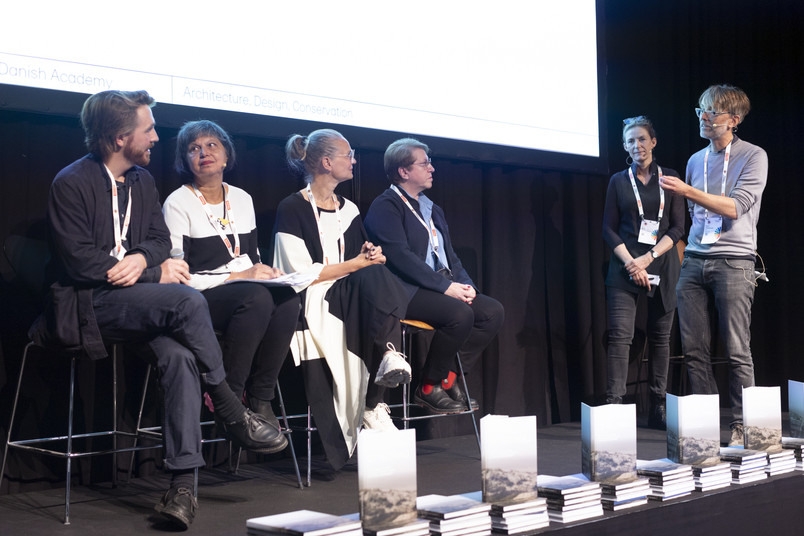 Panel discussion and presentation on stage with books displayed at the front.