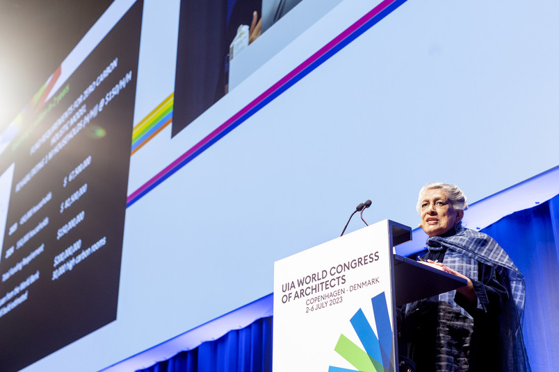 A speaker presenting at a podium at the UIA World Congress of Architects, with a large screen behind displaying slides.