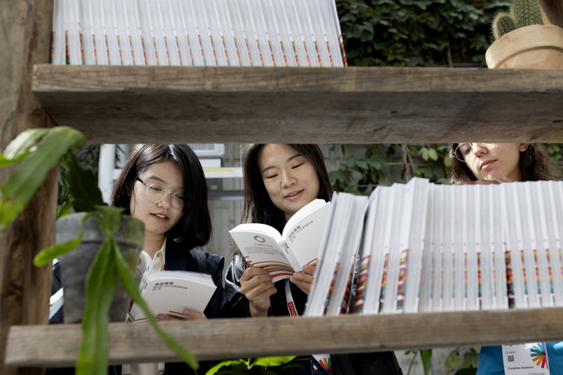 Visitors browsing and reading books on a display shelf in a green indoor setting.